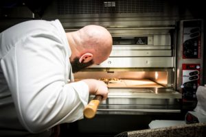 Image représentant un membre de l'équipe du Casa Leya, le chef consultant Ivano La Corte. Il est en train de mettre une pizza à cuire dans le four à pizza du restaurant.