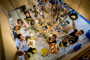 Image représentant une partie de l'équipe du restaurant. Ils se trouvent autour du citronnier de l'entrée. Ils tiennent un plat proposé par le Casa Leya dans leur main comme une pizza, des pâtes ou encore des salades.