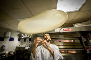 Image représentant un membre de l'équipe du Casa Leya, un cuisinier devant les fours a pizzas en train de former une pâte à pizza